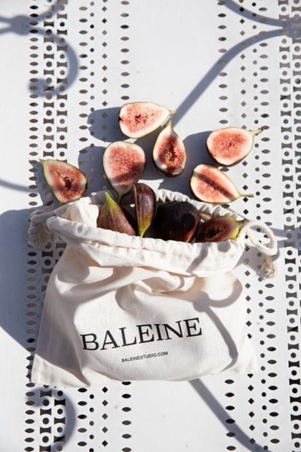 Fresh figs in a Baleine cotton bag on a patterned table in natural sunlight | Friske figner i en Baleine bomuldspose på et mønstret bord i naturligt sollys.